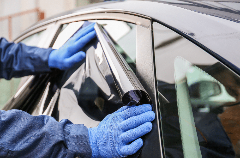 Employee with mobile tinting service applying window tint to car